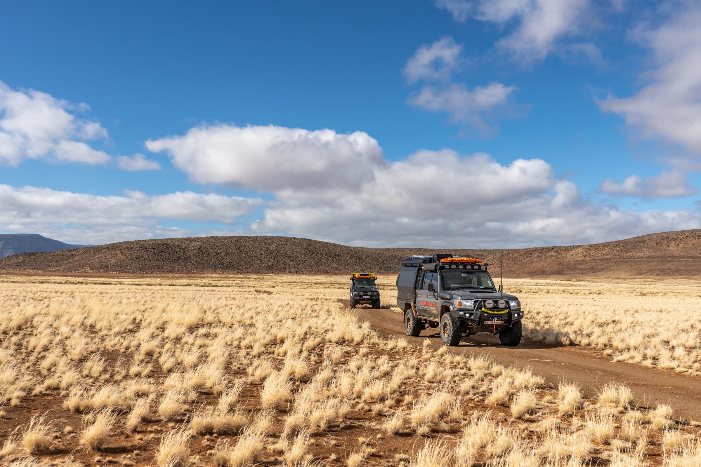 Two Bushtech-equipped Land Cruisers on a Karoo track under a wide cloudy sky