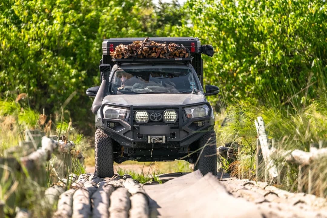 A Hilux with a Bushtech canopy crossing a log bridge