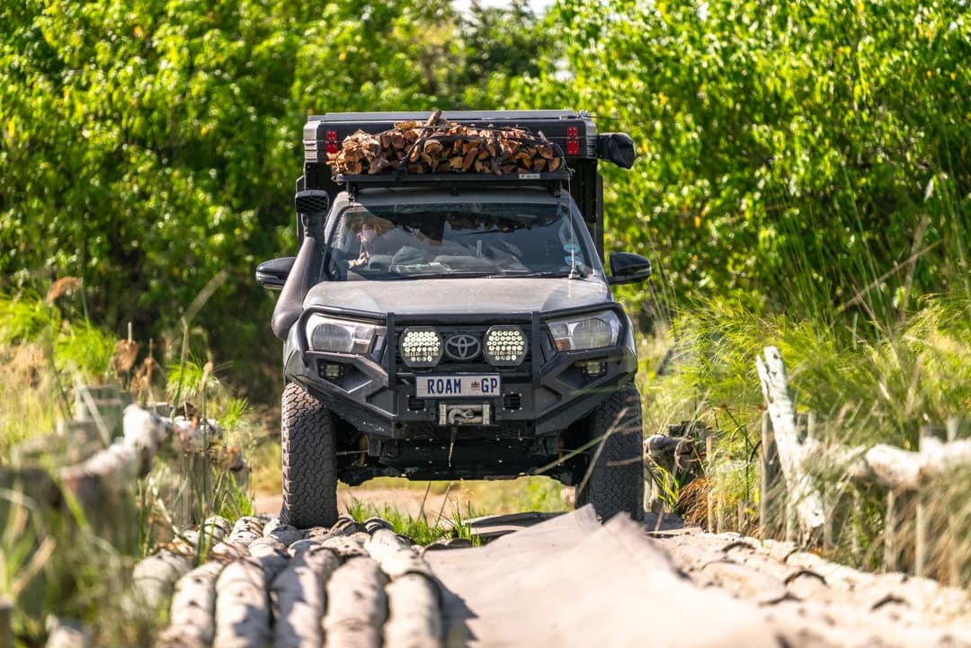 A Hilux with a Bushtech canopy crossing a log bridge